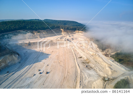 Aerial view of open pit mining of limestone materials for construction industry with excavators and dump trucks. Aerial view of open pit mining of limestone materials for construction industry with excavators and dump trucks. 86141164