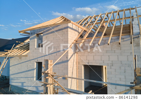Aerial view of unfinished frame of private house with aerated lightweight concrete walls and wooden roof frame under construction. Aerial view of unfinished frame of private house with aerated lightweight concrete walls and wooden roof frame under construction. 86141298