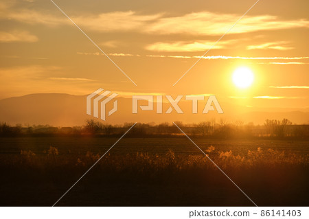 Beautiful evening panoramic landscape with bright setting sun over distant mountain peaks and asphalt road in front at sunset 86141403