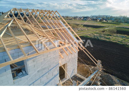 Aerial view of unfinished frame of private house with aerated lightweight concrete walls and wooden roof frame under construction. Aerial view of unfinished frame of private house with aerated lightweight concrete walls and wooden roof frame under construction. 86141560