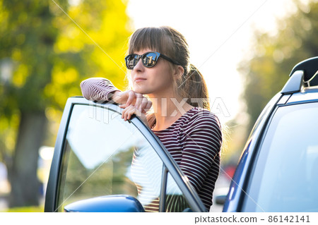Young female driver resting near her car enjoying warm summer day. Travel and getaway concept. 86142141
