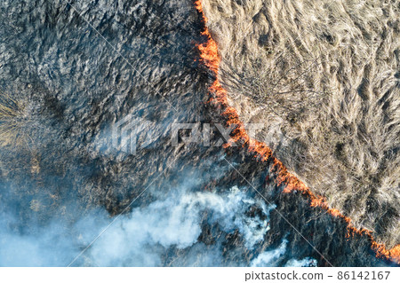 Aerial view of grassland field burning with red fire during dry season. Natural disaster and climate change concept Aerial view of grassland field burning with red fire during dry season. Natural disaster and climate change concept 86142167