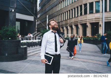 Cheerful businessman with tablet standing on street Cheerful businessman with tablet standing on street 86142482