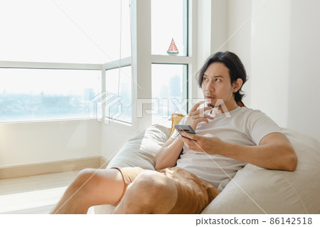 Man use smartphone while sit and relax on bean bag sofa in his apartment. 86142518