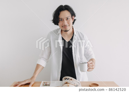 Man in white shirt reading magazine and drink coffee on wooden table. 86142520