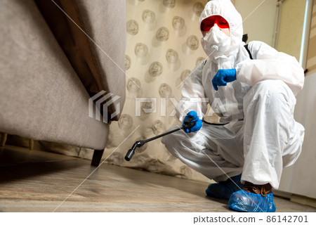 An exterminator in work clothes sprays pesticides with a spray gun. Fight against insects in apartments and houses. Disinsection of the premises An exterminator in work clothes sprays pesticides with a spray gun. Fight against insects in apartments and houses. Disinsection of the premises 86142701
