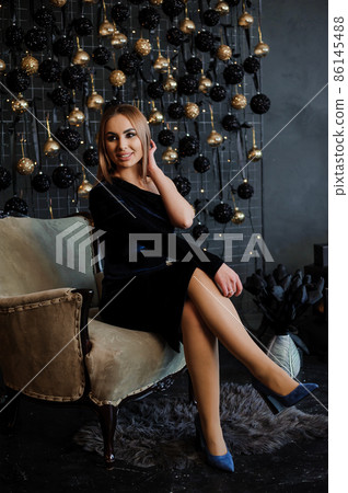 A girl in a beautiful dress sits on a chair, black and gold balloons in the background 86145488