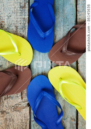 stack of several pairs of multi-colored rubber flip flops on a blue wooden background stack of several pairs of multi-colored rubber flip flops on a blue wooden background 86145636