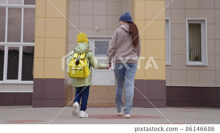affectionate mother leads the child back to school, to teach first lessons of childhood, a school student goes hand in hand with mom, happy family, a cheerful boy son with mom go to school building 86146686