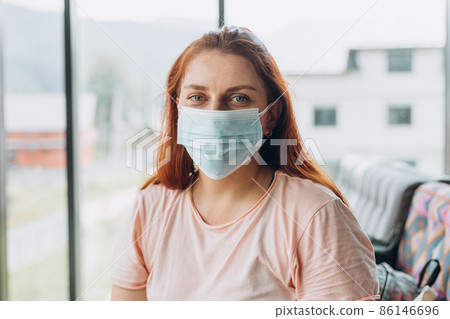 A happy woman in a protective medical mask on her face sits at the airport waiting for a flight, social distance concept. A happy woman in a protective medical mask on her face sits at the airport waiting for a flight, social distance concept. 86146696