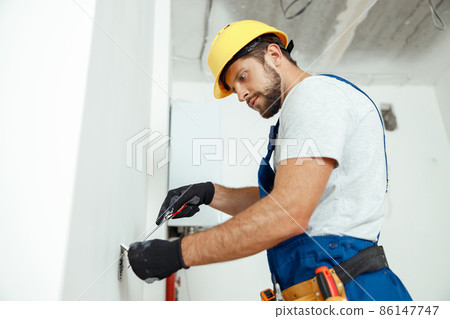 Male worker professional electrician in uniform installing electrical outlet in apartment after renovation work Male worker professional electrician in uniform installing electrical outlet in apartment after renovation work 86147747