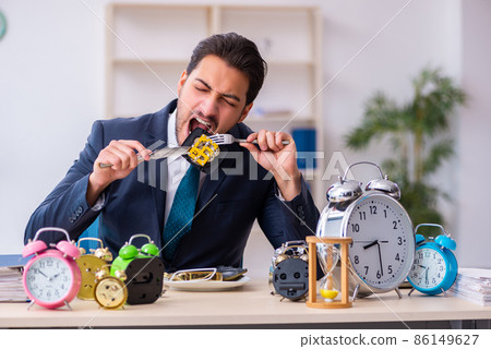 Young businessman employee eating alarm-clock Young businessman employee eating alarm-clock 86149627