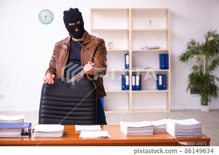 Young man in balaclava stealing information from the office 86149634