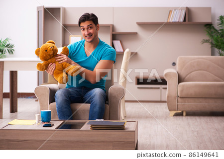 Young man sitting with bear toy at home Young man sitting with bear toy at home 86149641