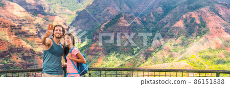 Hawaii nature hiking travel couple tourists taking selfie at Waimea Canyon lookout viewpoint. Summer vacation travelers enjoying outdoor activity in Kauai, hawaiian islands Hawaii nature hiking travel couple tourists taking selfie at Waimea Canyon lookout viewpoint. Summer vacation travelers enjoying outdoor activity in Kauai, hawaiian islands 86151888