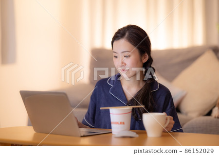 Living room at night A woman eating cup ramen while looking at a computer 86152029