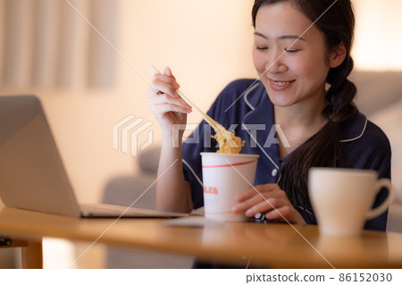 晚上的客廳 一個女人一邊看著電腦一邊吃杯拉麵 86152030