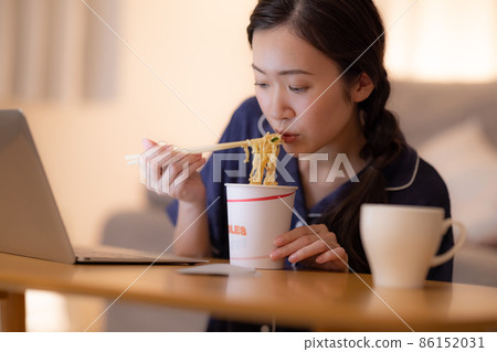 Living room at night A woman eating cup ramen while looking at a computer 86152031