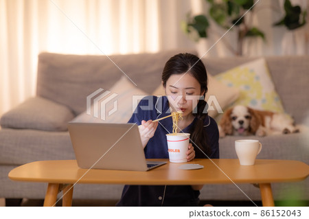 晚上的客廳 一個女人一邊看著電腦一邊吃杯拉麵 86152043
