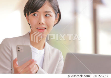 Business woman who holds a smartphone and moves her eyes with a smile 1 86153267