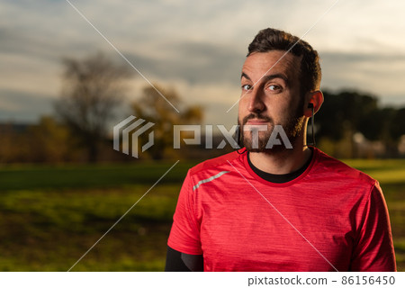 Confident runner listening to music in earphones in park Confident runner listening to music in earphones in park 86156450