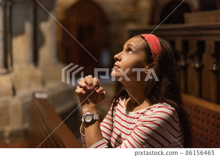 Hispanic woman praying with clasped hands in cathedral Hispanic woman praying with clasped hands in cathedral 86156465