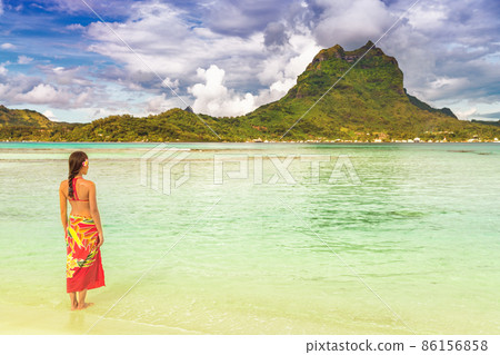 Sun tropical beach luxury travel vacation tourist woman relaxing wearing red pareo cover up skirt as beachwear in Tahiti. View of Bora bora island from private motu. Sunshine and ocean Sun tropical beach luxury travel vacation tourist woman relaxing wearing red pareo cover up skirt as beachwear in Tahiti. View of Bora bora island from private motu. Sunshine and ocean 86156858