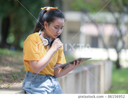 A teenage woman looks down at the tablet in her hand with a worried expression. A teenage woman looks down at the tablet in her hand with a worried expression. 86156952