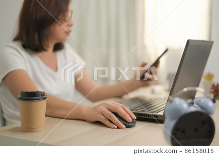 A woman hand holding on a mouse using a laptop working from home. 86158018