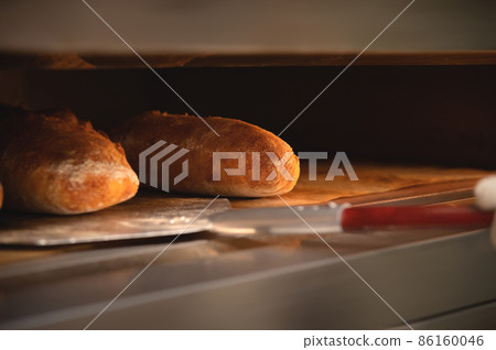 Close-up of a baker's shovel taking freshly baked artisan bread out of the oven. Bread production with copy space Close-up of a baker's shovel taking freshly baked artisan bread out of the oven. Bread production with copy space 86160046