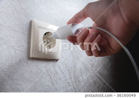 Close-up of a woman's hand inserting a white usb charger into a 220 volt socket Close-up of a woman's hand inserting a white usb charger into a 220 volt socket 86160049