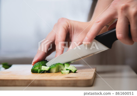 Close-up of female hands cutting cucumbers for a vegan salad. Home cooking healthy and wholesome food Close-up of female hands cutting cucumbers for a vegan salad. Home cooking healthy and wholesome food 86160051
