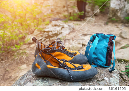 Orange climbing shoes and magnesium in a blue bag stand on a stone. Climbing clothing Orange climbing shoes and magnesium in a blue bag stand on a stone. Climbing clothing 86161203