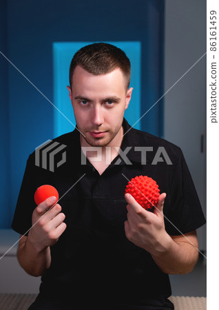 Attractive Caucasian young male masseur holding two massage balls in his hands and looking into the camera. Choice of instruments for self-massage 86161459