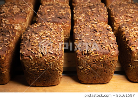 A lot of whole delicious homemade rectangular rye bread with sunflower seeds on top lies on a wooden rack background 86161597