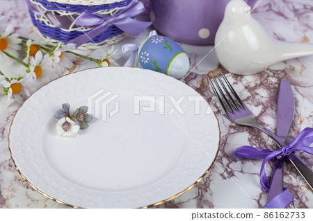 Easter table setting and dinner with yellow flowers, festive decorations, white bird and multicolored eggs. 86162733