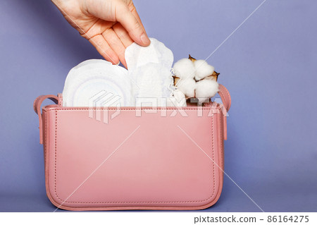 Women's hand takes out panty liner from pink cosmetic bag with tampons and feminine sanitary pads 86164275