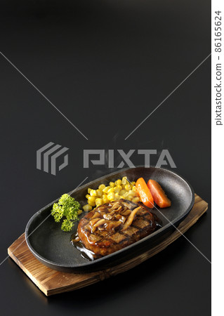 Hot Japanese-style hamburger steak with parsley, carrot glass, corn, and mushroom sauce on an iron plate on a black background 86165624