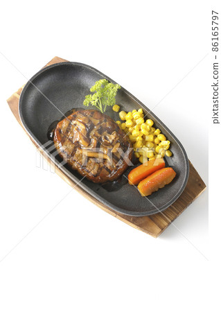 A bird's-eye view of a hot Japanese-style hamburger steak with parsley, carrot glass, corn, and mushroom sauce on an iron plate on a white background. A bird's-eye view of a hot Japanese-style hamburger steak with parsley, carrot glass, corn, and mushroom sauce on an iron plate on a white background. 86165797