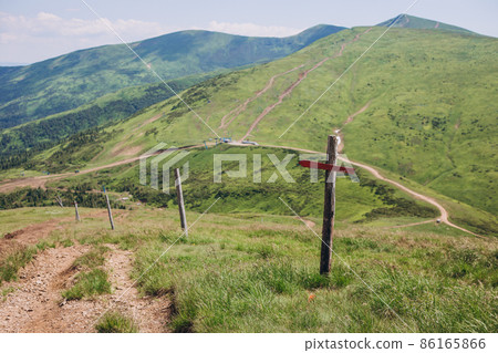 One wooden red signpost in the summer mountain with copyspace. Conceptual leading indicator. Old Arrow on the wooden signpost pointing to a direction. One wooden red signpost in the summer mountain with copyspace. Conceptual leading indicator. Old Arrow on the wooden signpost pointing to a direction. 86165866