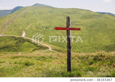 One wooden red signpost in the summer mountain with copyspace. Conceptual leading indicator. Old Arrow on the wooden signpost pointing to a direction. 86165867