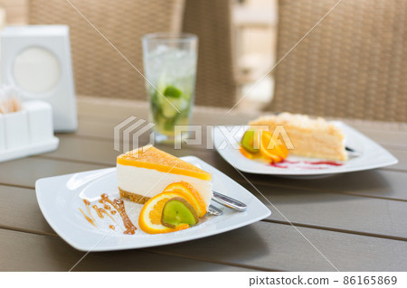 Slice of classic cheesecake with caramel topping. Piece of cake on ceramic white plate on wooden table in cafe. Food banner. Several slices of delicious desserts, restaurant menu concept 86165869