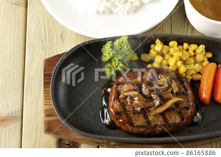 熱日式漢堡牛排配歐芹、玻璃、玉米和蘑菇醬在鐵板上、清湯和米飯 熱日式漢堡牛排配歐芹、玻璃、玉米和蘑菇醬在鐵板上、清湯和米飯 86165886
