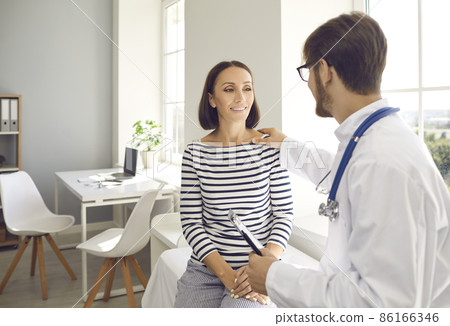 Friendly male doctor touches female patient's shoulder for encouragement, empathy and support during medical examination. Concept of trust, medical ethics, good news and healthcare. 86166346