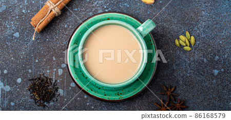 Indian tea hot drink with milk and spices in rustic green teacup with ingredients for making masala chai Indian tea hot drink with milk and spices in rustic green teacup with ingredients for making masala chai 86168579