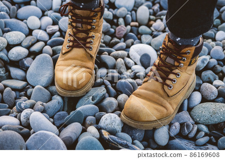 Legs in yellow rough hiking boots on the pebble beach. Travel concept. 86169608