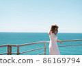 Young woman in white dress and hat stands by the sea. 86169794