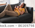 Young woman lying on the couch and using smartphone for speak with friends and relatives. 86169798