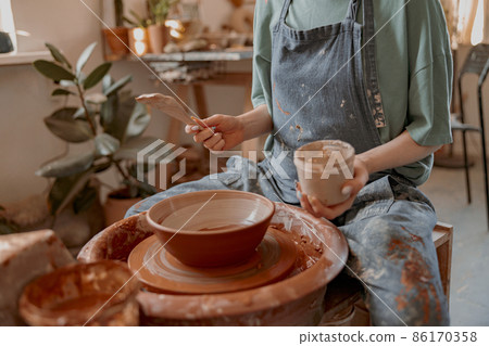 Skillful female potter engaged in craft in her workshop Skillful female potter engaged in craft in her workshop 86170358