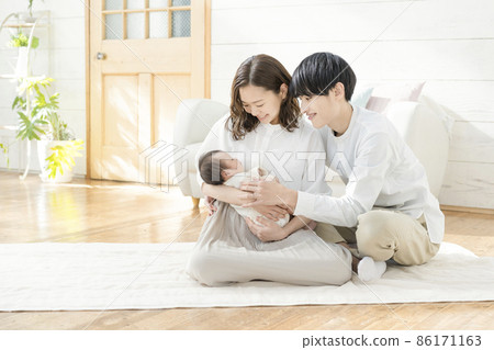Portrait of a young mom, dad and three babies sitting in the living room and smiling Portrait of a young mom, dad and three babies sitting in the living room and smiling 86171163
